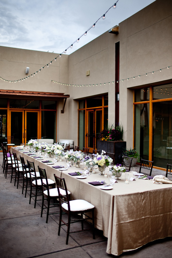 outdoor reception table setting with gold tablecloth, purple, white, and yellow centerpieces, and hanging accent lights - photo by New Mexico based wedding photographers Twin Lens
